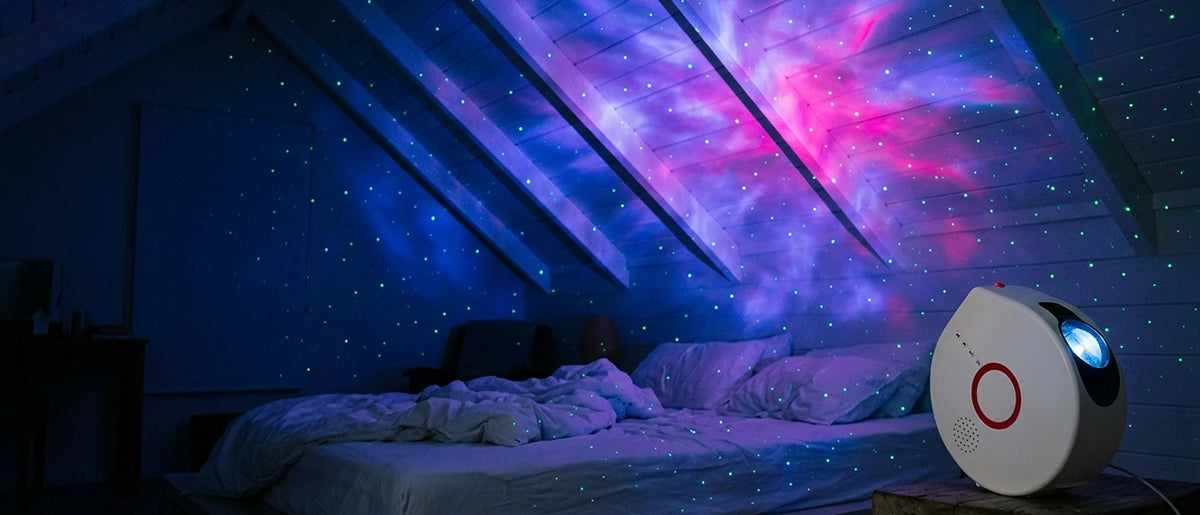 A bedroom at night shot from the foot of a made bed, the whole ceiling and the far wall covered in a blue-violet nebula with green stars, the projector on the nightstand at the right